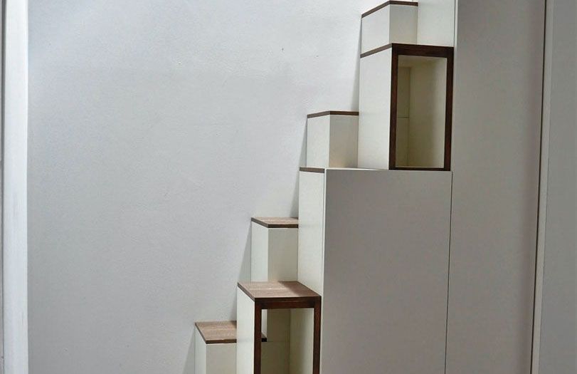 Scala minimalista con gradini bianchi e dettagli in legno su una parete liscia.