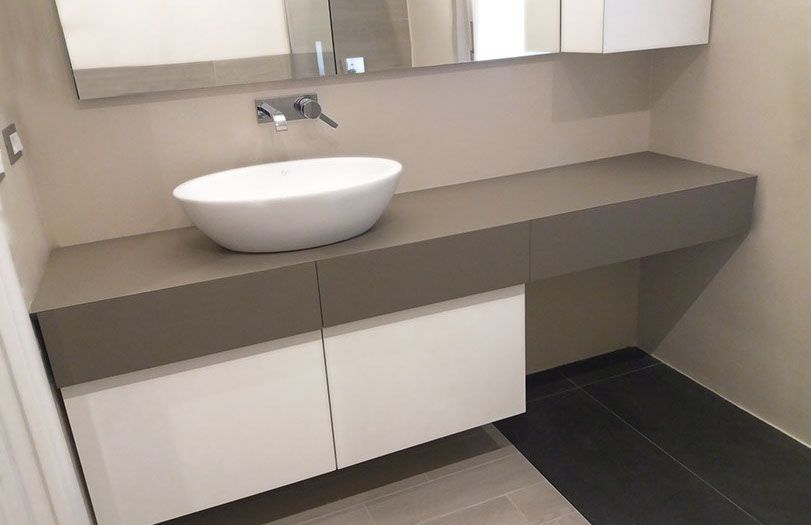 Mobile bagno moderno con lavabo a ciotola bianco, ampio specchio e piano e ante grigi.