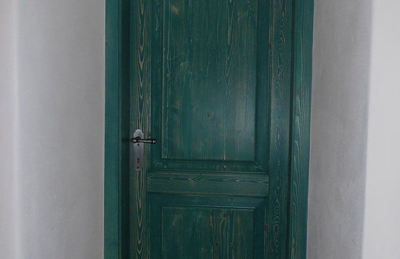 Porta di legno verde con maniglia argentata tra pareti bianche