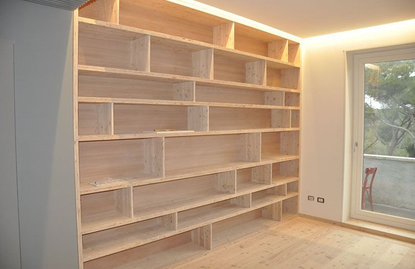 Librerie in legno a incasso con illuminazione a LED calda in una stanza moderna e vuota vicino a una porta a vetri.