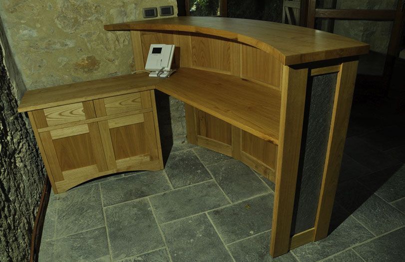 Bancone reception in legno curvato con un piccolo terminale per computer sulla parte superiore, posizionato su un pavimento in piastrelle di pietra.