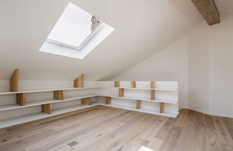Luminosa mansarda con lucernario, pareti bianche, travi in ​​legno e scaffalature a muro.