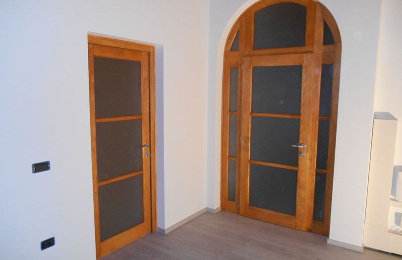 Angolo di stanza vuoto con due porte ad arco in legno e pareti di colore chiaro.