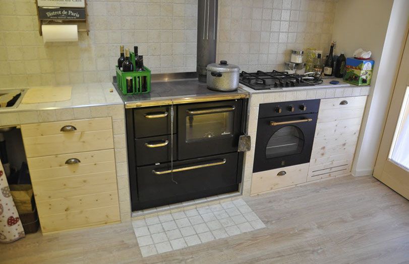 Una cucina moderna con forno nero, piano cottura a gas, paraschizzi piastrellato di bianco e mobili in legno chiaro.