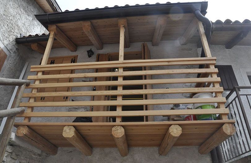 Balcone rustico in legno con ringhiera a doghe e supporti in tronchi, situato all'esterno di una casa.