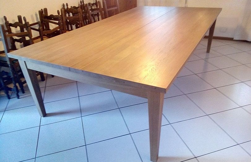 Tavolo da pranzo in legno in una stanza piastrellata con sedie impilate sullo sfondo.