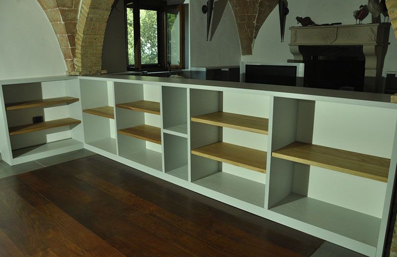 Mobile a muro bianco con ripiani in legno in una stanza vuota con pavimento in parquet.