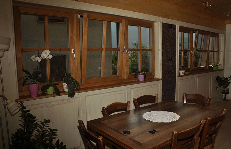 Sala da pranzo con tavolo e sedie in legno accanto alle finestre e piante in vaso.