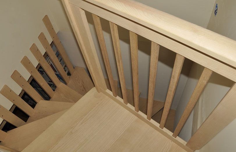 Pianerottolo di una scala in legno con ringhiere in legno chiaro e pareti beige, visto dall'alto.