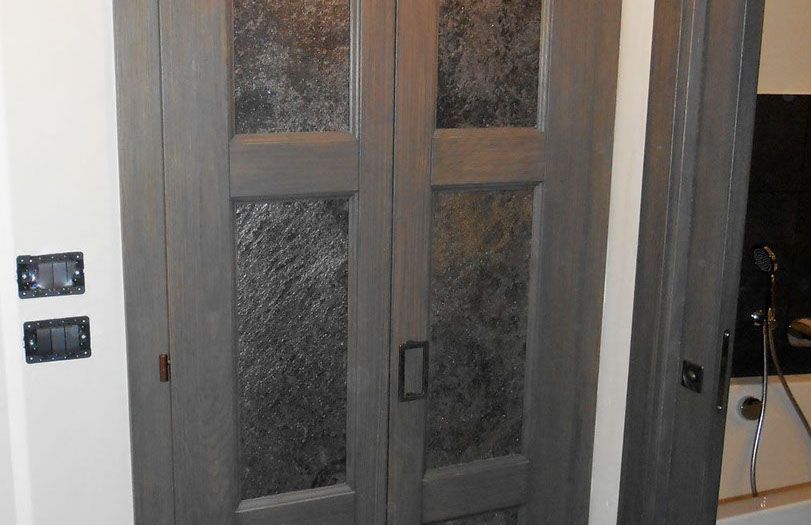 In un corridoio si trovano due doppie porte grigie con pannelli in vetro satinato e interruttori a parete sulla sinistra.