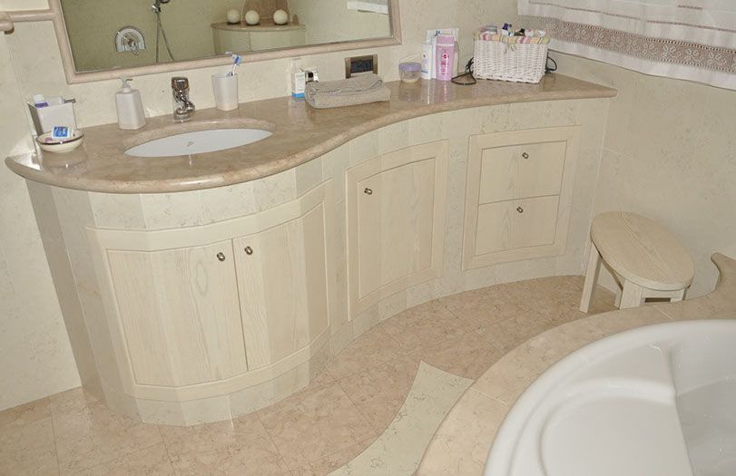 Bagno color crema con mobile lavabo curvo, doppio lavabo, specchio e vasca da bagno parzialmente a vista.