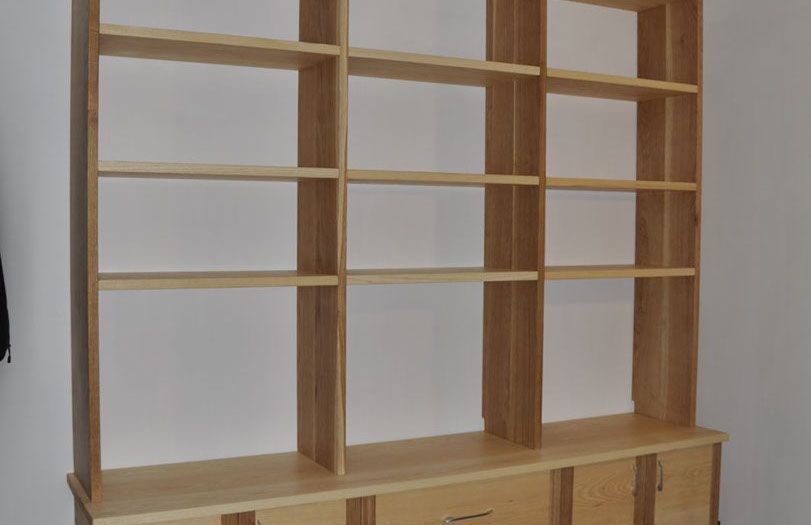 Scaffale in legno vuoto addossato a una parete bianca, con cassetti nella parte inferiore e vani a giorno.