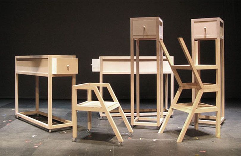 Prototipi di mobili in legno disposti in un'officina, tra cui tavoli, sgabelli e strutture alte simili a sedie.