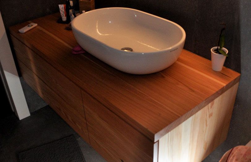 Lavabo moderno su mobiletto in legno con vasca bianca e piccola pianta in vaso.