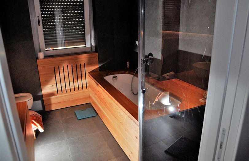 Bagno moderno con vasca da bagno con dettagli in legno, doccia in vetro e pavimento in piastrelle scure.