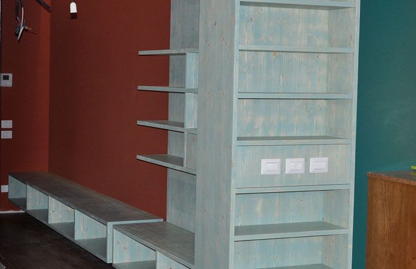 Soggiorno moderno con scaffalature a muro, mobili in legno chiaro e una lunga panca bassa addossata a una parete rossa.