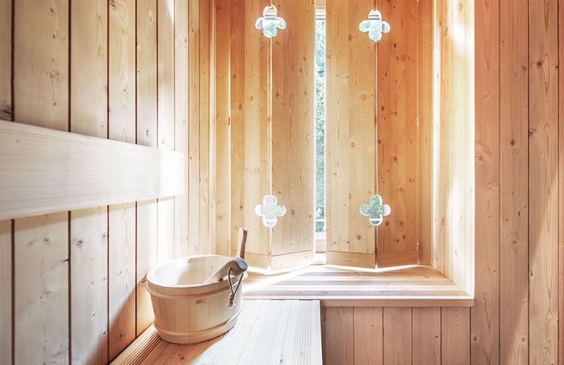 Sauna rivestita in legno con panca in legno, secchio e finestra satinata con vetri a forma di croce.