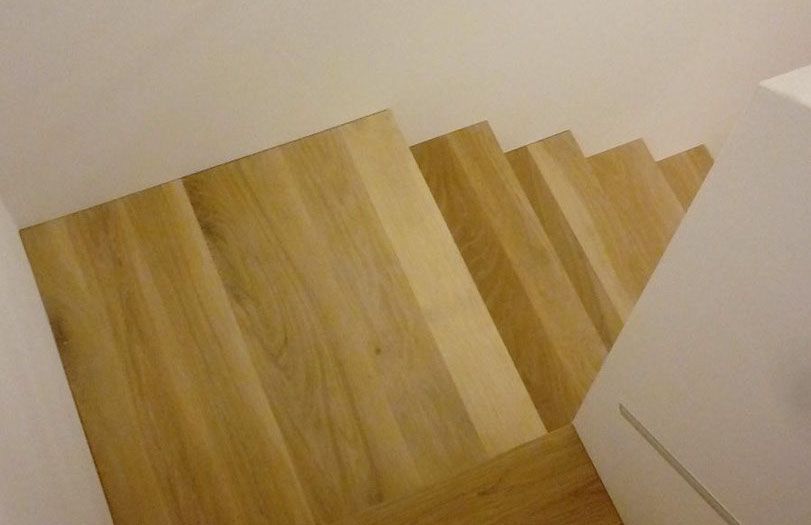 Scala in legno vista dall'alto, con pareti bianche e pianerottolo visibili.