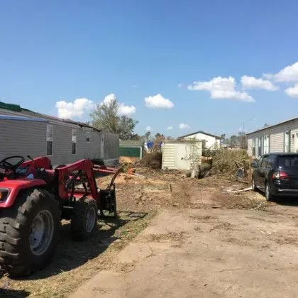 A tractor clearing debris between mobile homes after a storm.