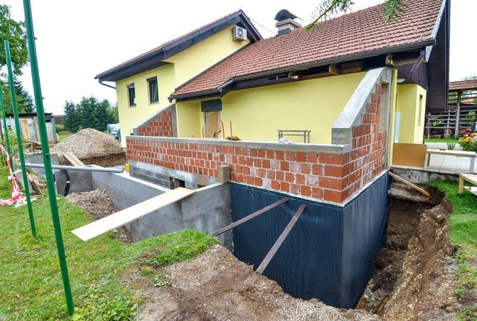 Partially built house with exposed brick, yellow walls, and a dark foundation on a muddy construction site