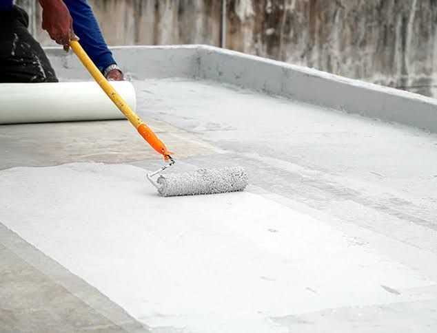 Person applying white waterproof coating with a roller on a flat roof surface