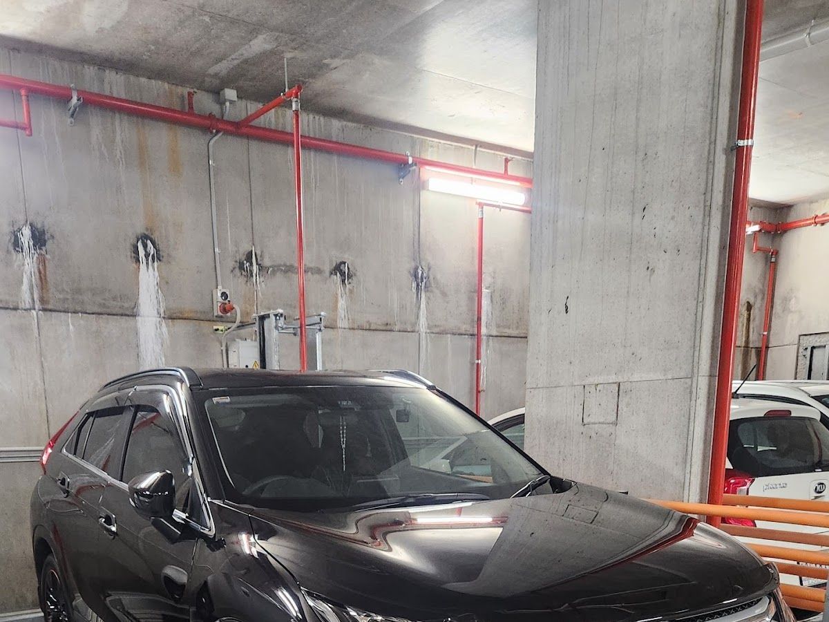 Black SUV parked in an indoor concrete garage with red pipes and a white car in the background