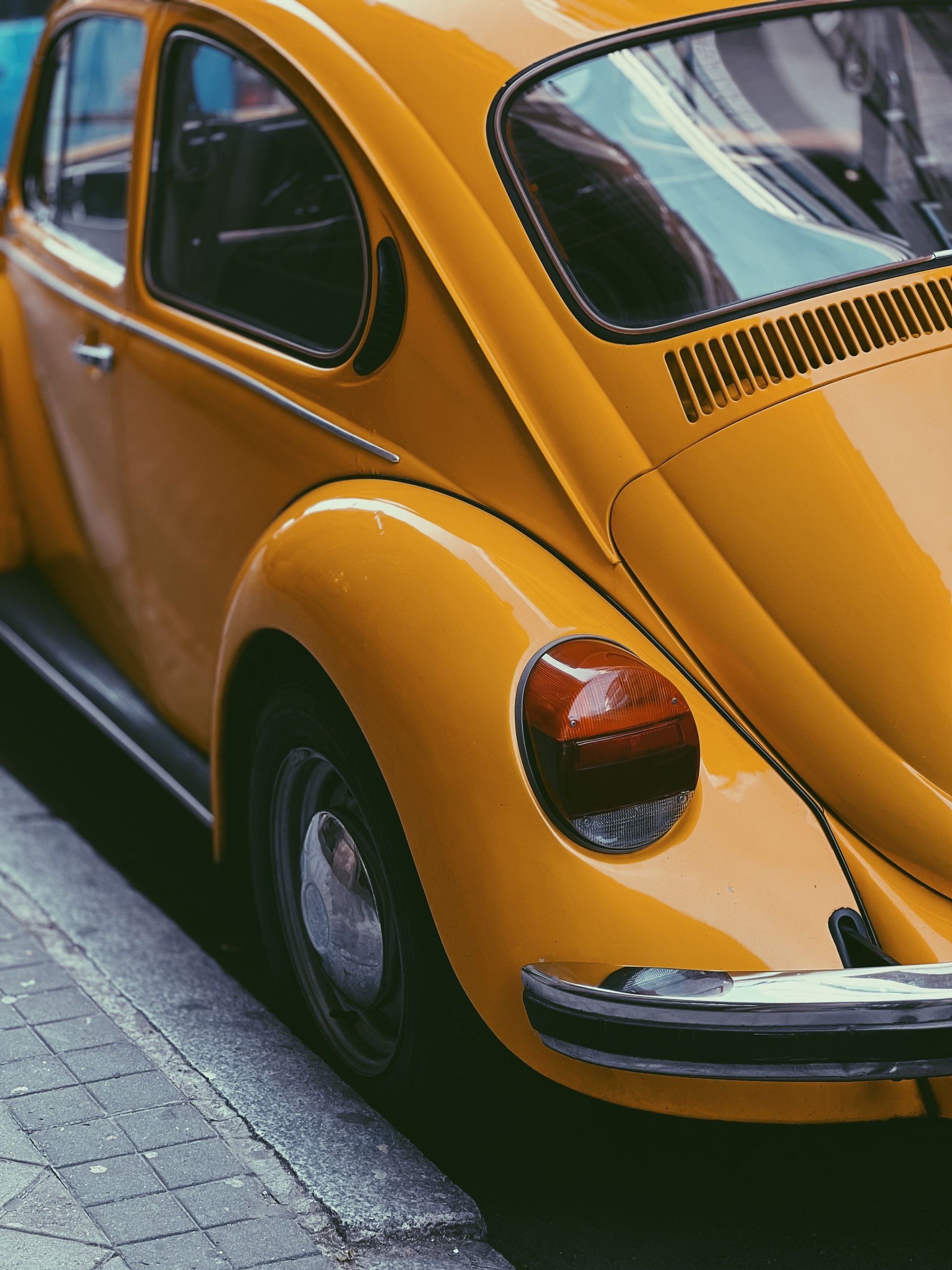 Yellow vintage Volkswagen Beetle parked on a street, viewed from the rear side.