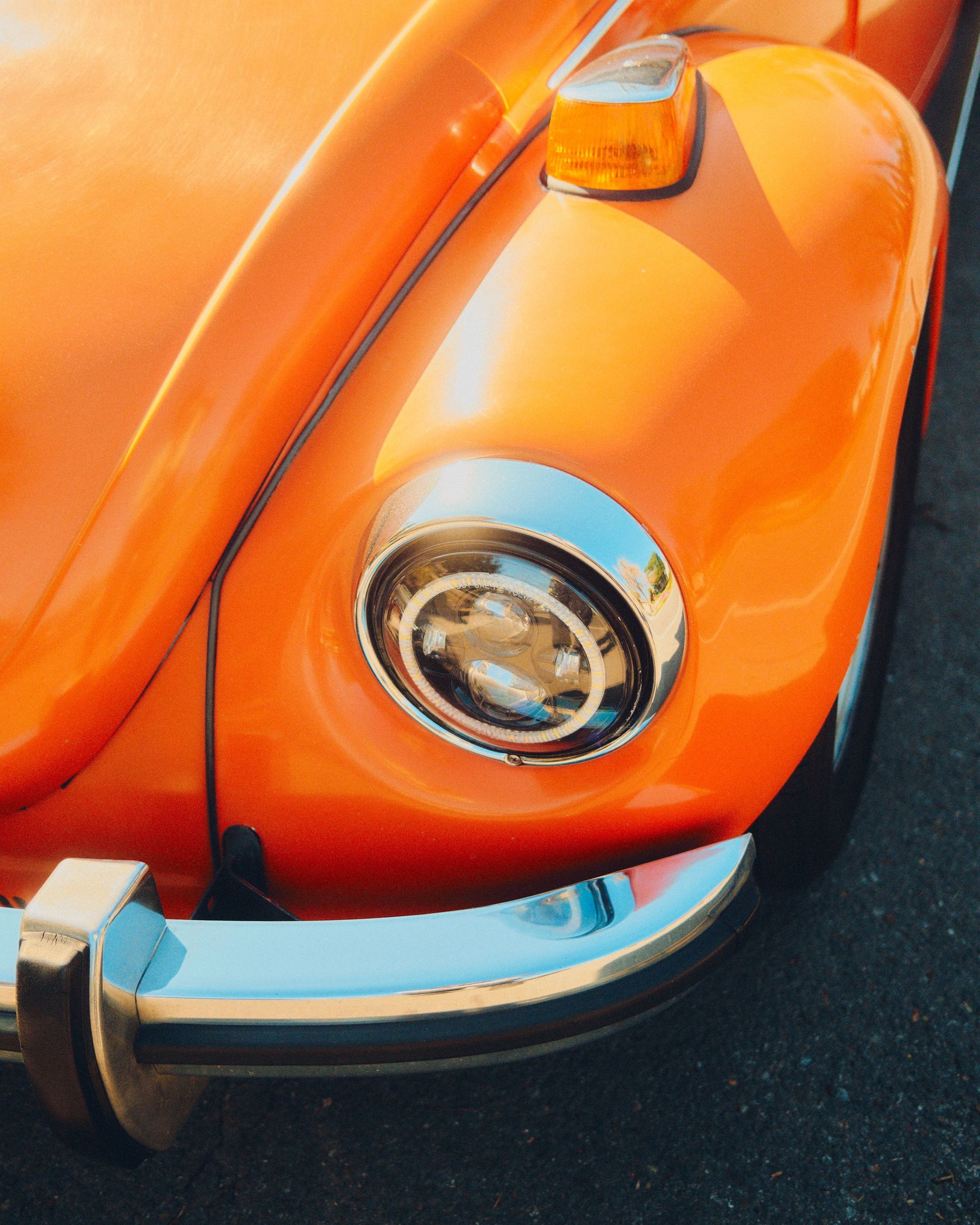 Close-up of an orange vintage car’s front fender, headlight, and chrome bumper