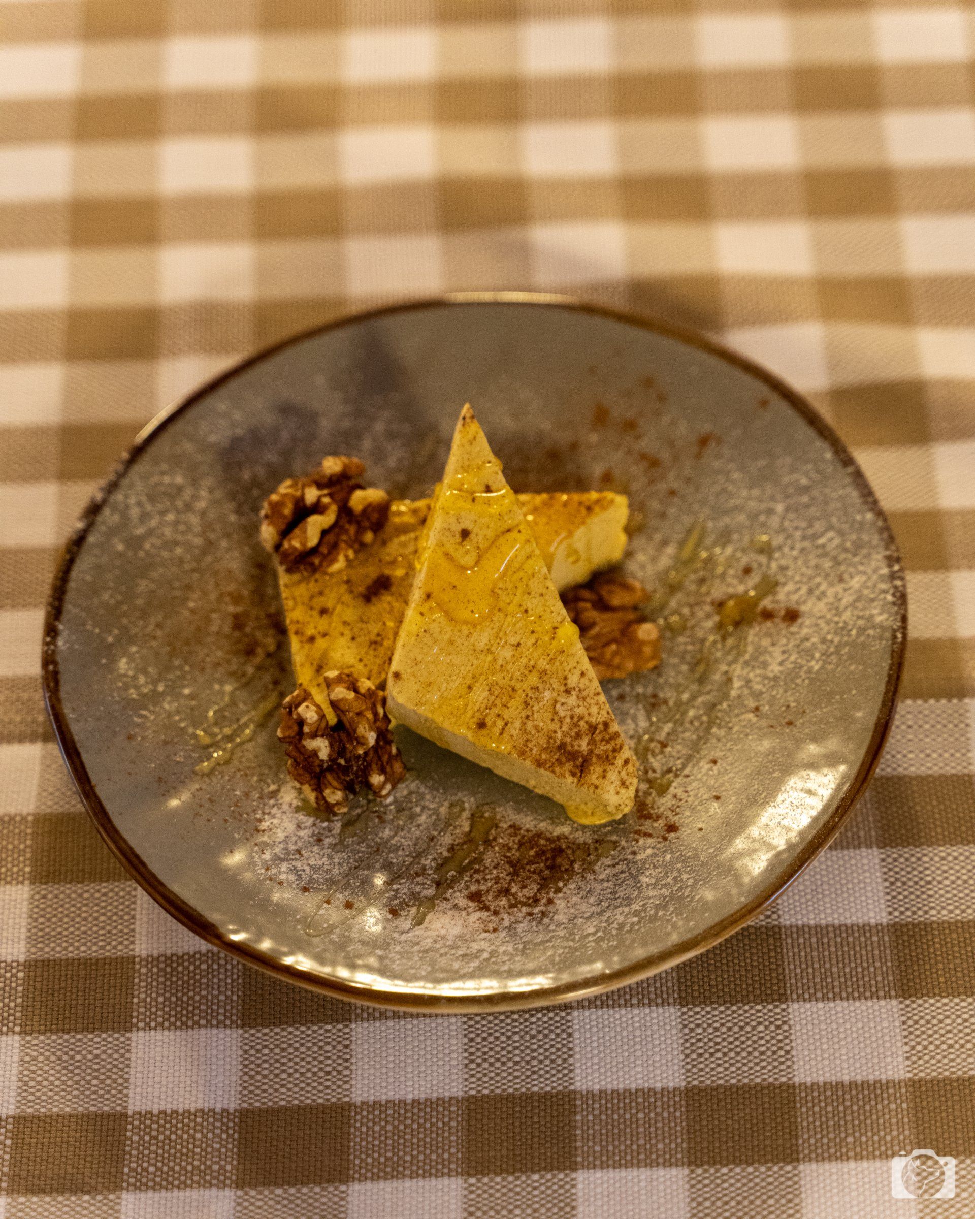 Dessert su un piatto blu: due fette triangolari con noci e polvere su un tavolo a scacchi.