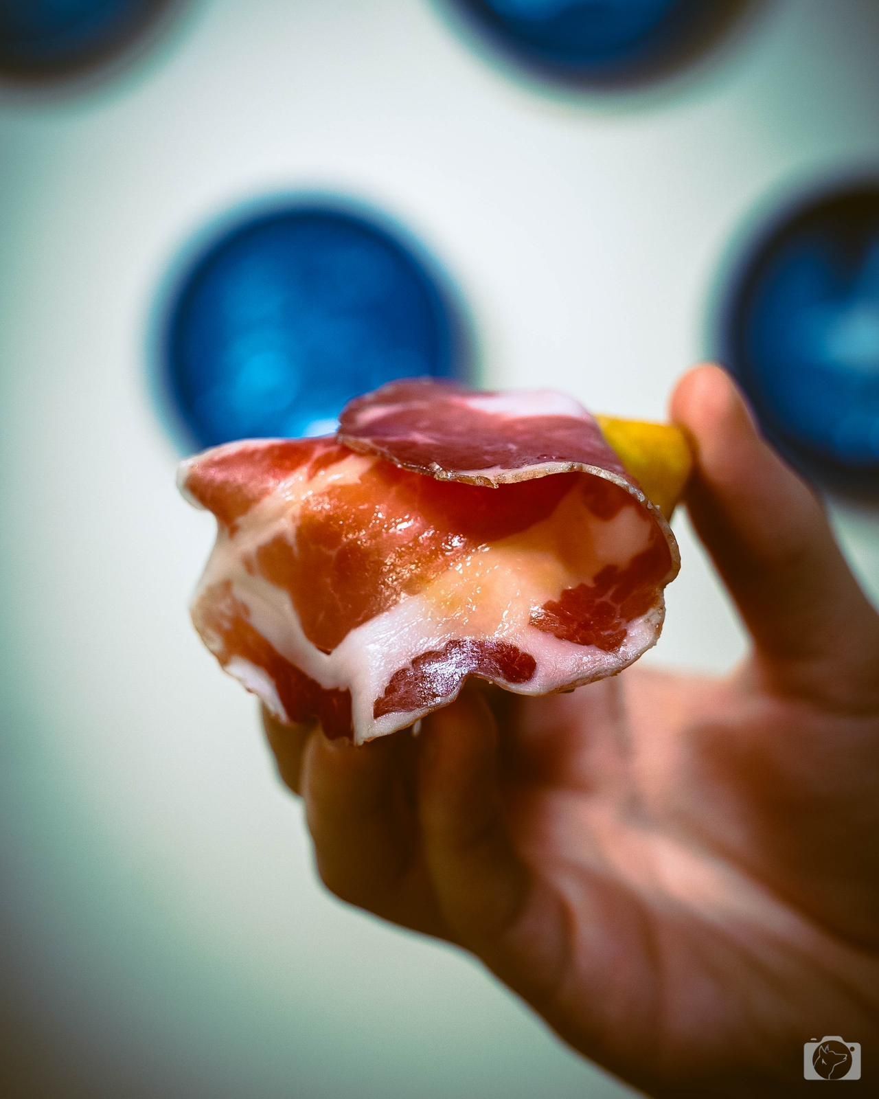Mano che tiene un boccone di cibo: prosciutto e formaggio, su sfere blu.