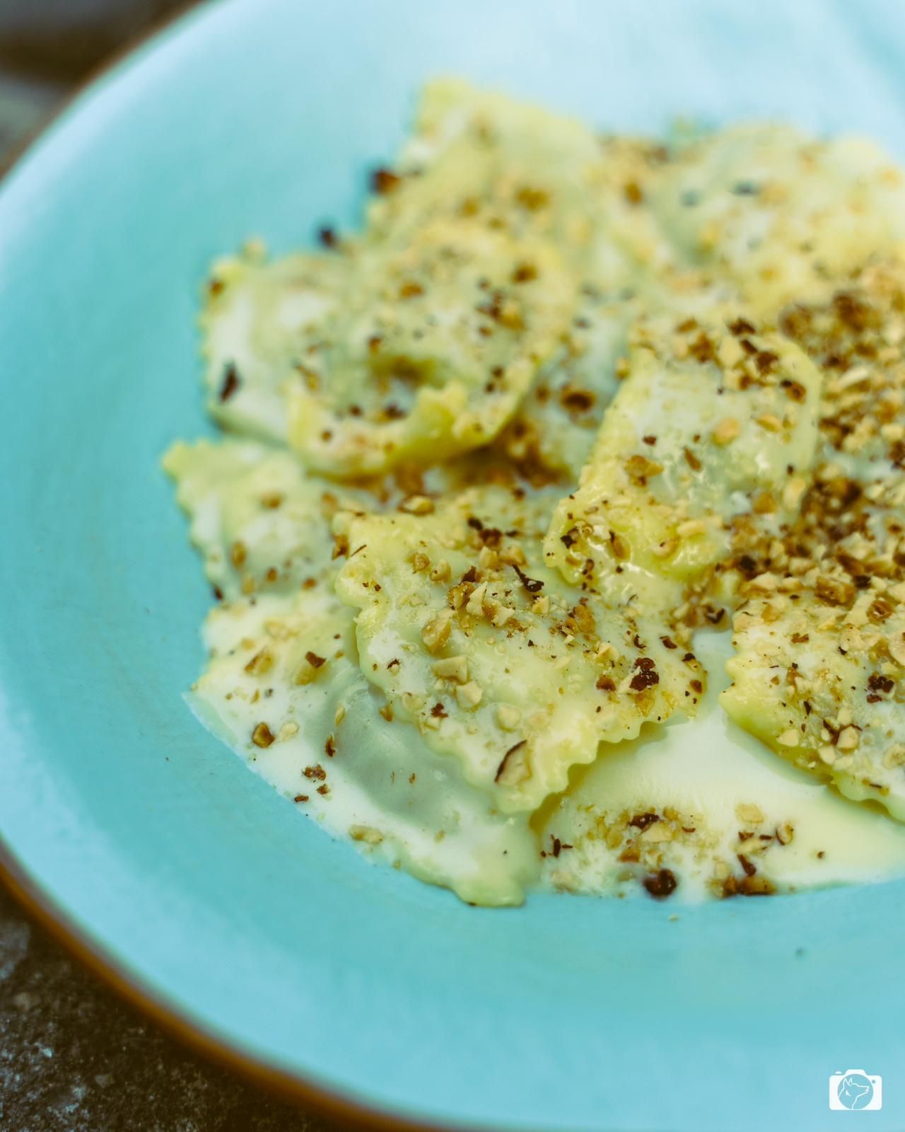 Ravioli in salsa cremosa con noci, serviti in una ciotola turchese.