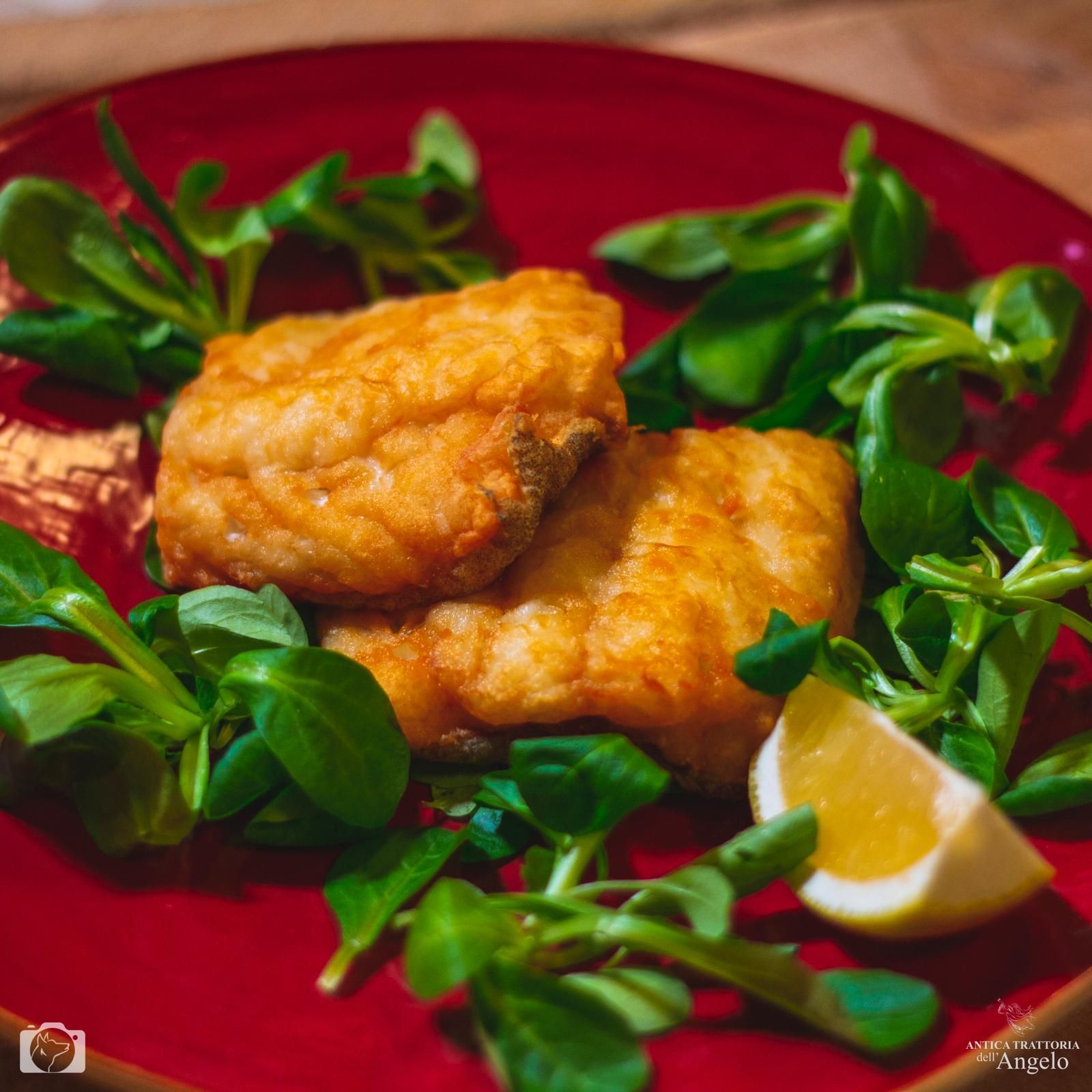 Filetti di pesce fritti su un piatto rosso con lattuga verde e spicchio di limone.