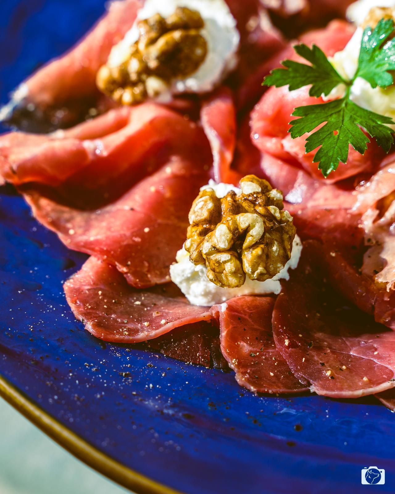 Antipasto di carpaccio con noci e crema di formaggio su un piatto blu.