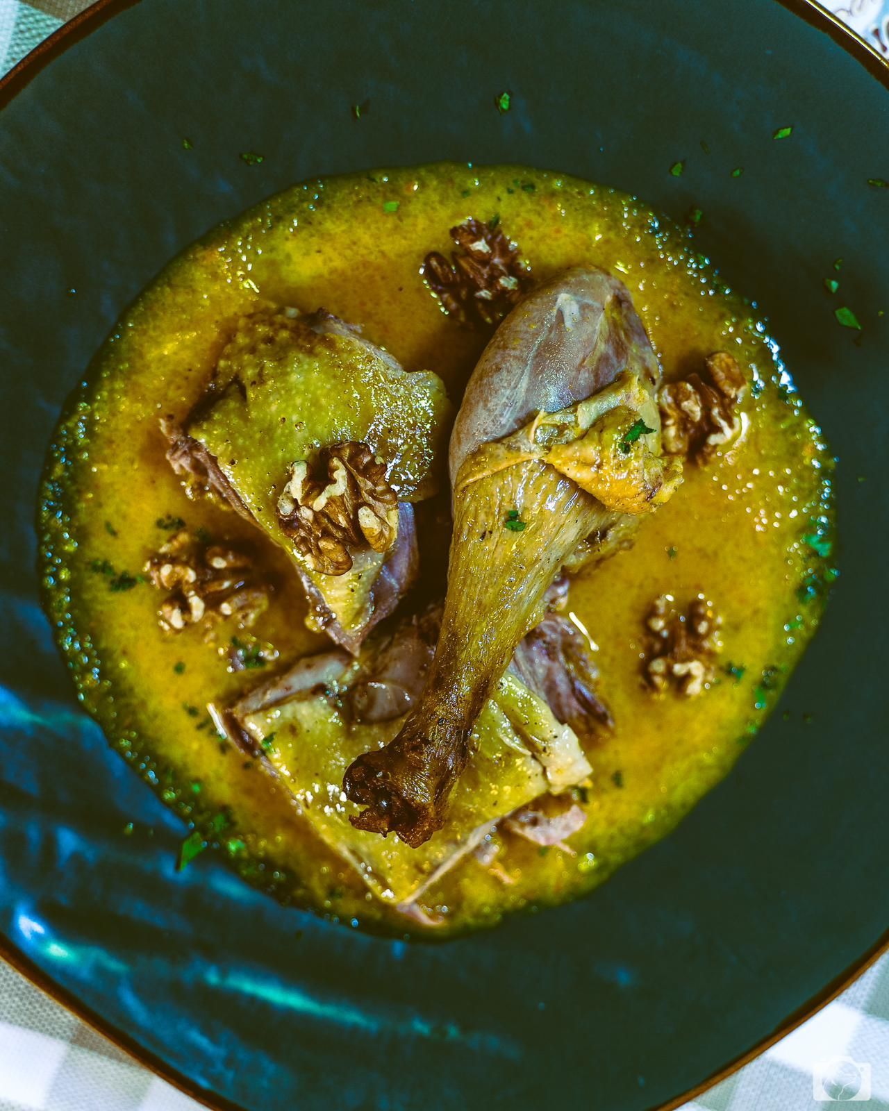 Anatra in salsa gialla, guarnita con noci, servita su un piatto scuro.