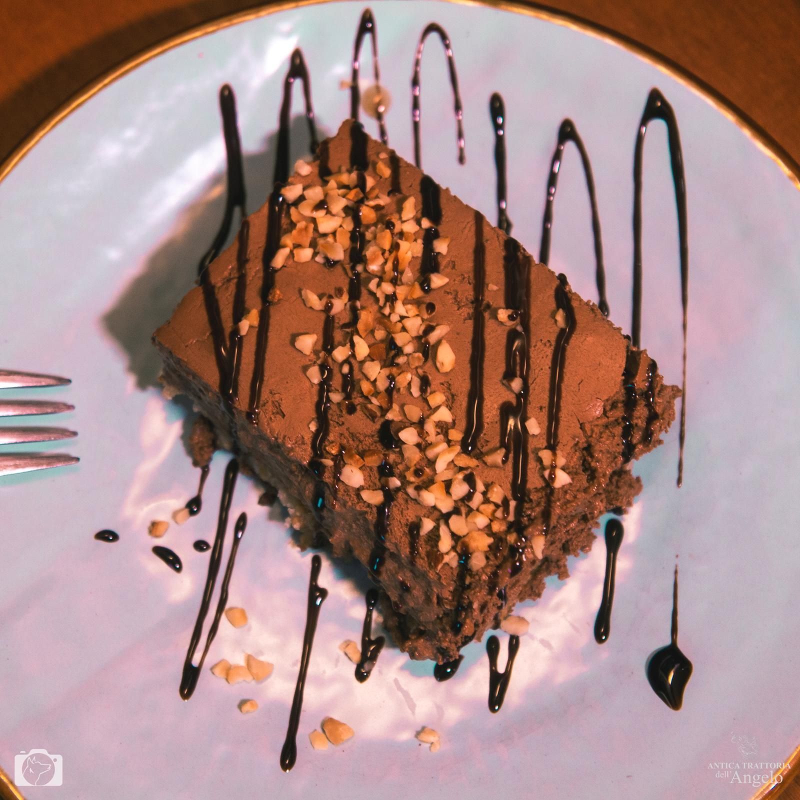 Fetta di dessert al cioccolato su un piatto blu, condita con salsa al cioccolato e guarnita con noci.