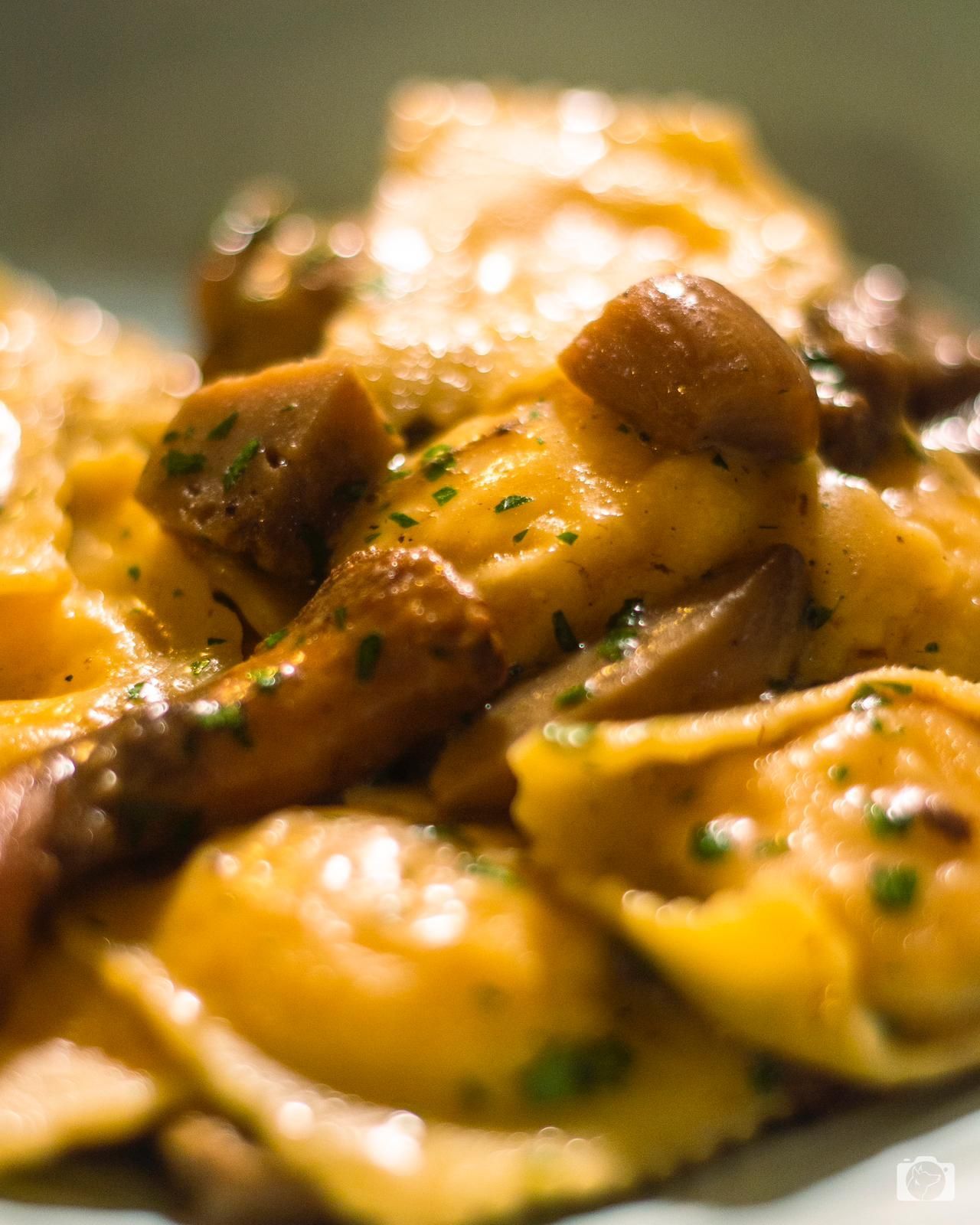 Ravioli ai funghi, primo piano. Pasta gialla con funghi marroni, cosparsa di erbe aromatiche.