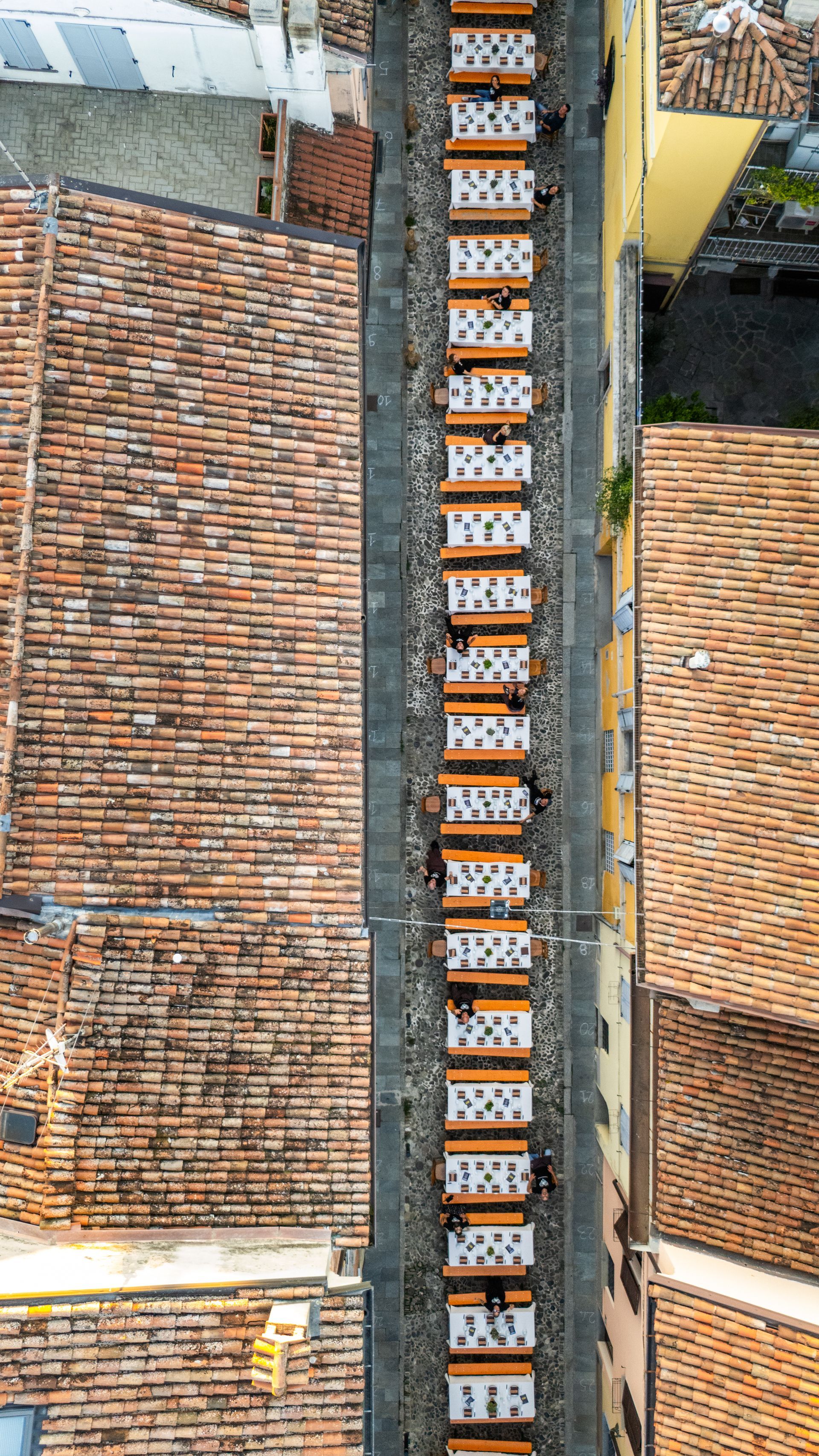 Vista dall'alto di una stretta strada fiancheggiata da balconi tra edifici con tetti in terracotta.