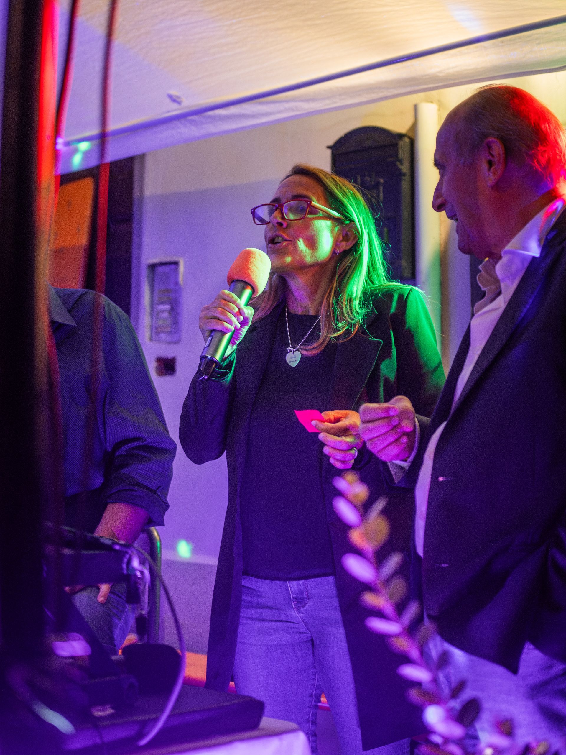 Donna che canta al microfono; uomo accanto a lei. Ambientazione notturna, luci colorate.