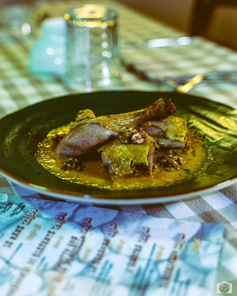 Piatto di cibo con carne in salsa gialla, su una tovaglia a quadri; sullo sfondo si vedono il bicchiere e il menu.