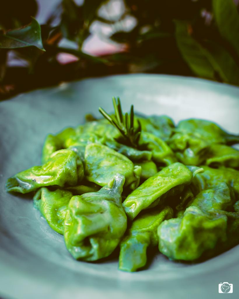 Piatto di pasta verde con rametto di rosmarino su un piatto di ceramica.