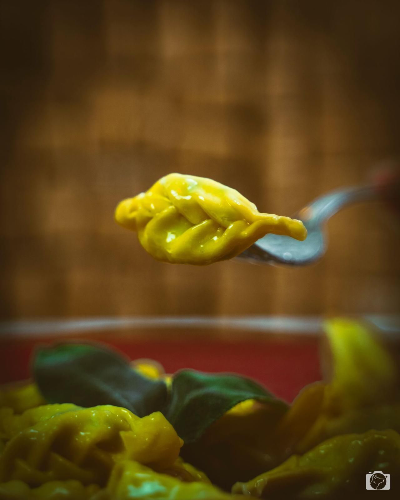 Ravioli gialli infilzati su una forchetta, tenuti sopra una ciotola di ravioli gialli e verdi.