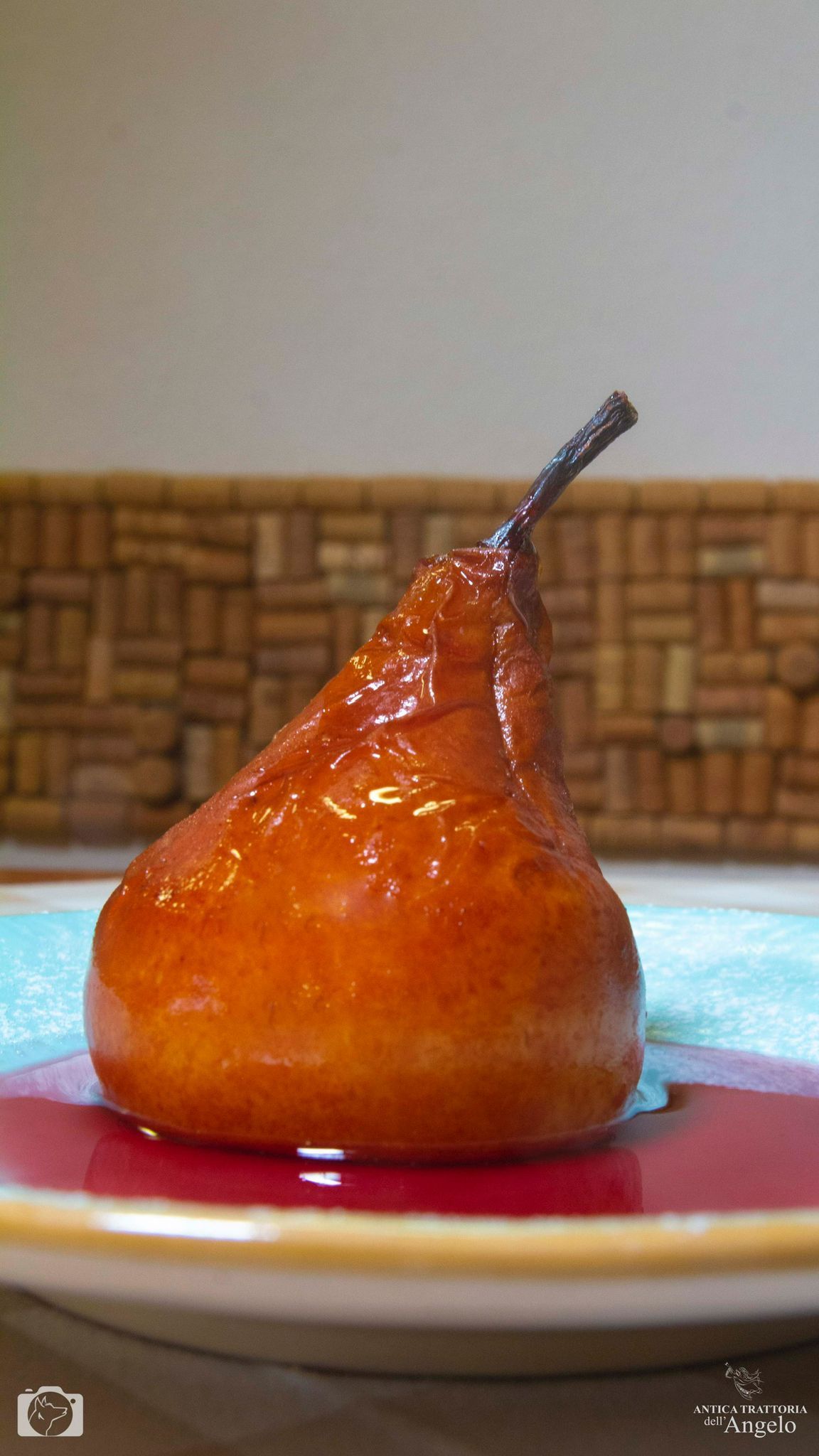 Pera caramellata su un piatto blu e rosso. Marrone e lucida, con gambo scuro, su uno sfondo di sughero.