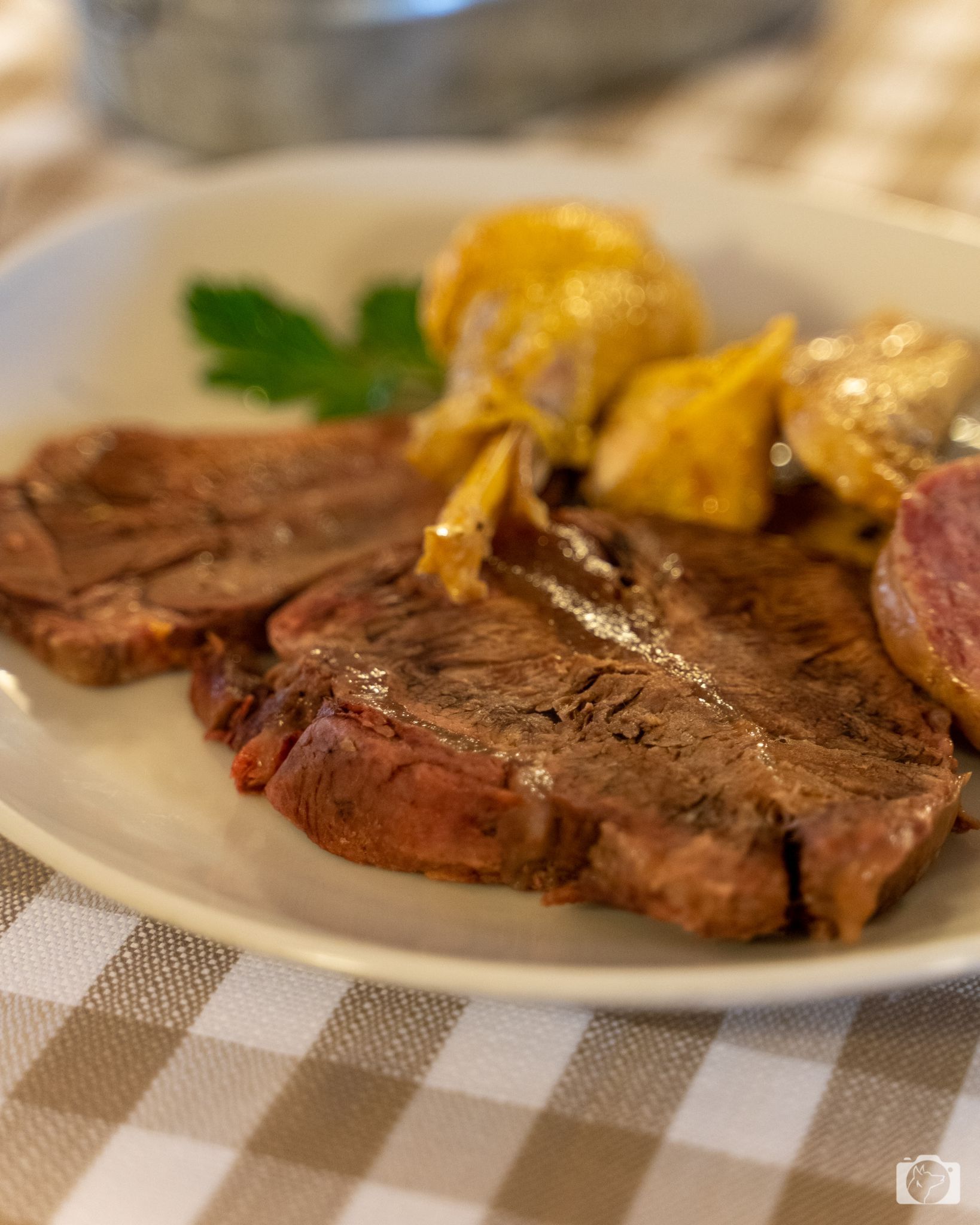 Piatto con bistecca cotta, patate e salsiccia, su una tovaglia a quadri.