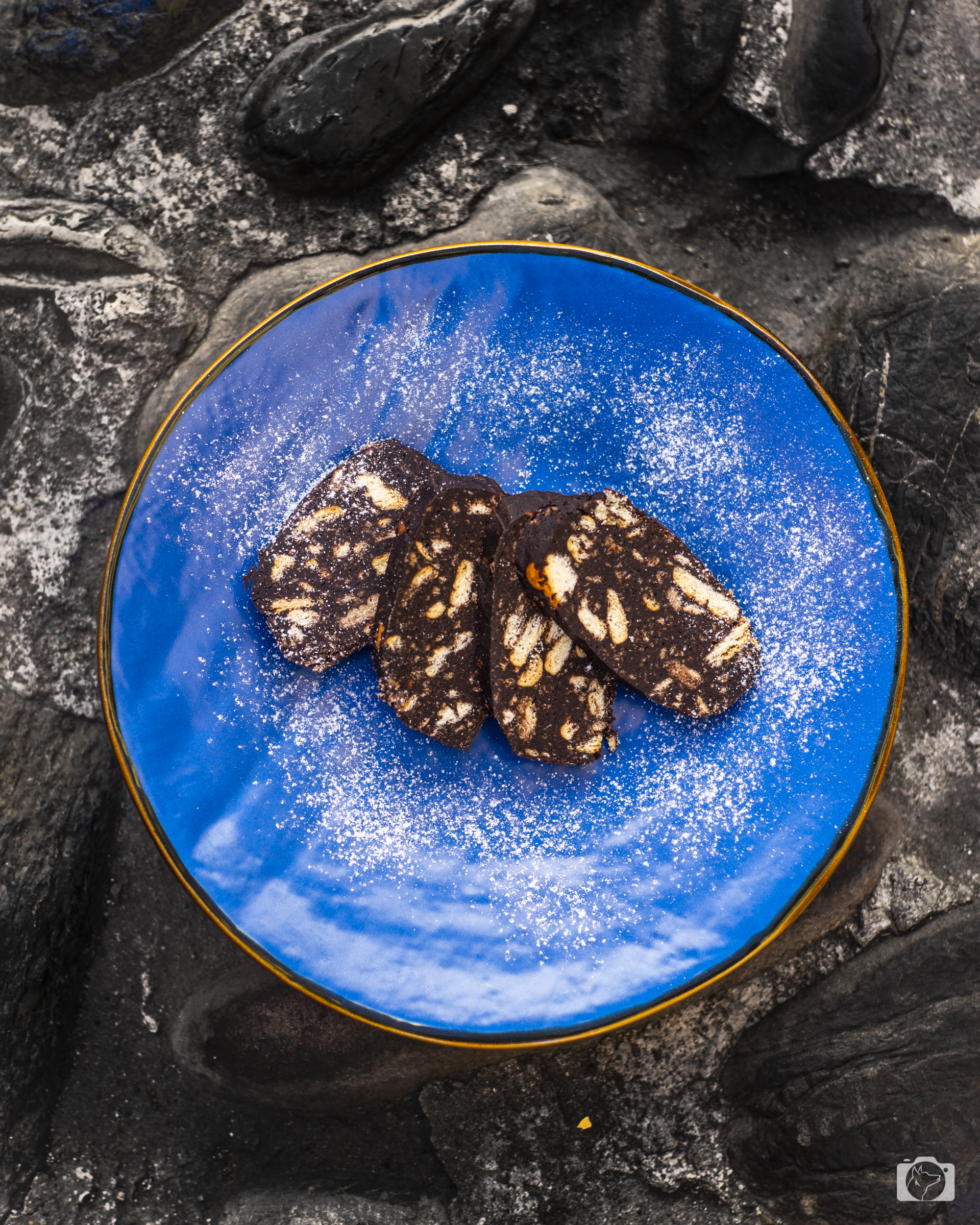 Quattro fette di biscotto al cioccolato con zucchero a velo su un piatto blu, su uno sfondo di pietra.