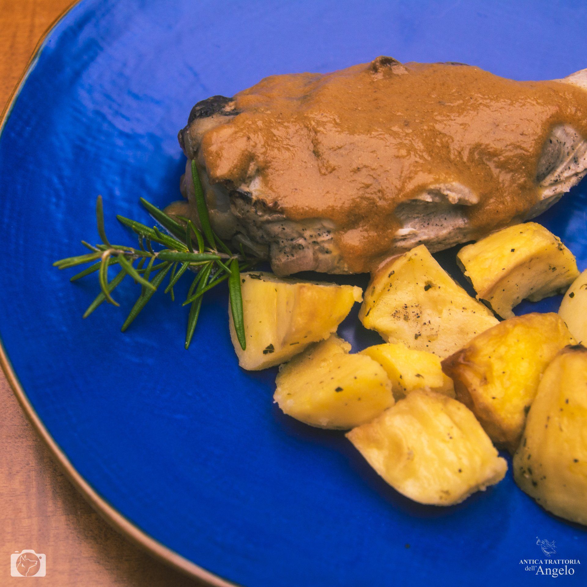 Carne arrosto con sugo e patate su un piatto blu, rametto di rosmarino.