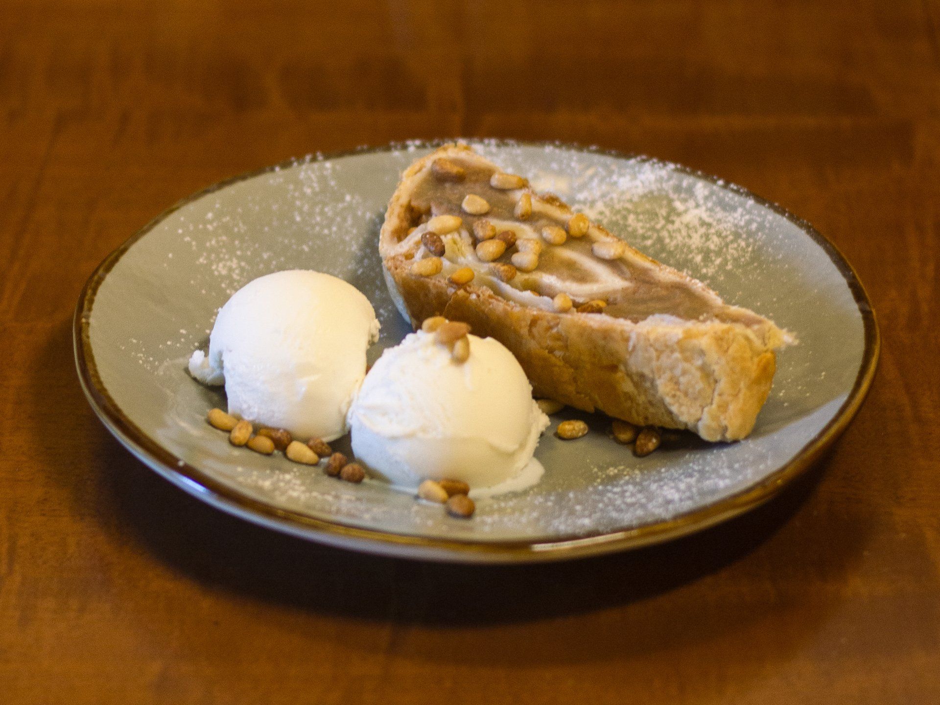 Strudel di mele con gelato e pinoli su un piatto, spolverato con zucchero a velo.