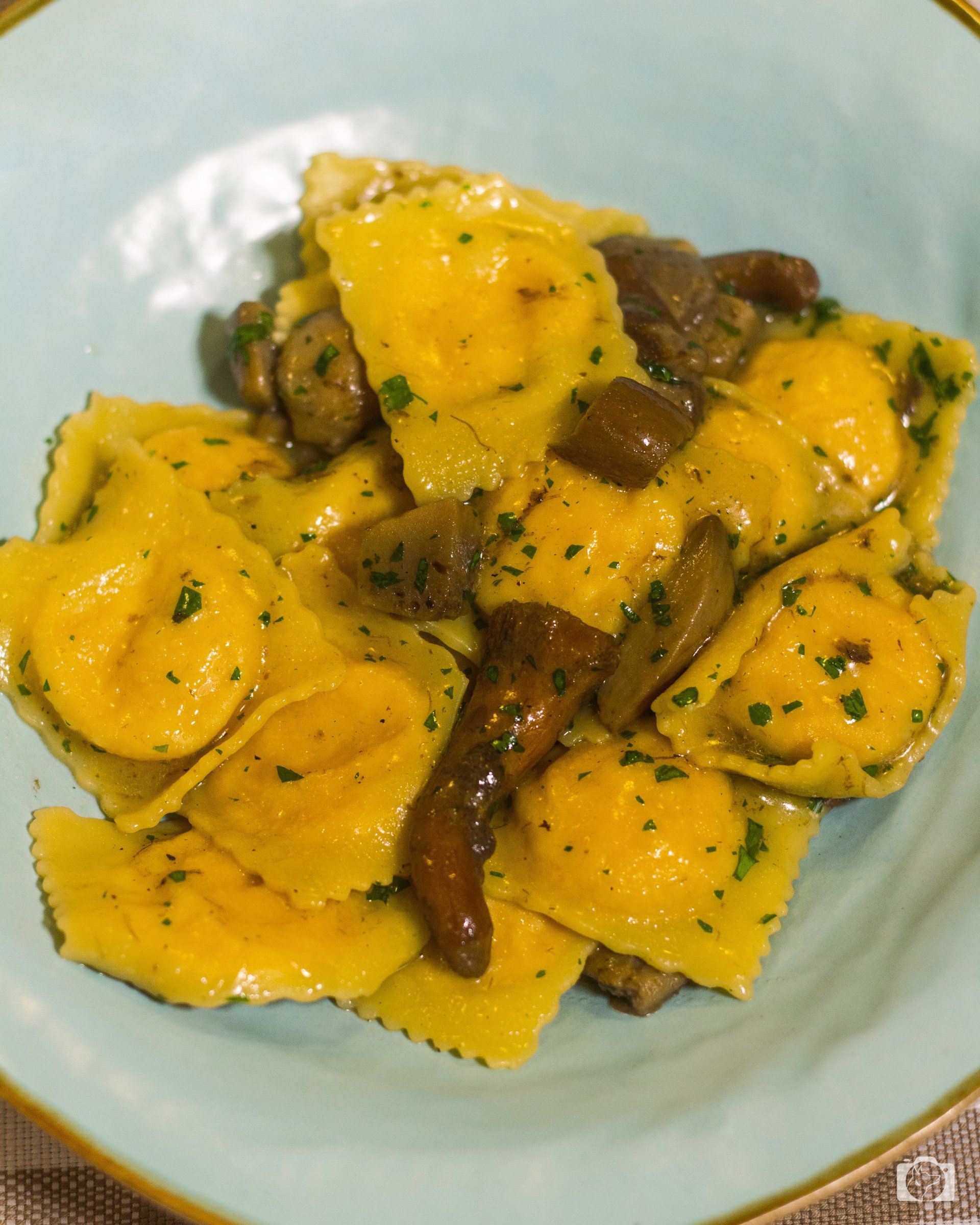 Ravioli di pasta con funghi e prezzemolo, serviti in una ciotola azzurra.
