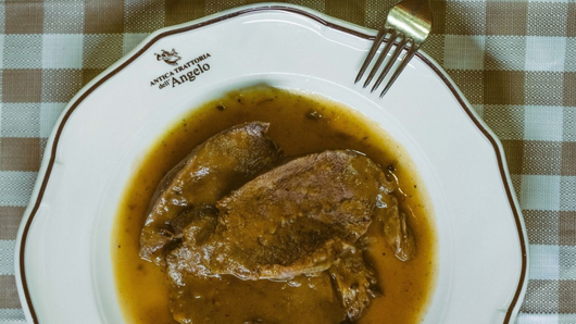 Tavolo apparecchiato per un pasto al ristorante: piatto di barbabietole, cestino del pane, bicchiere di vino e stoviglie su una tovaglia a quadri.