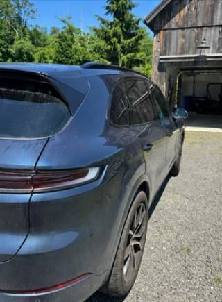 Dark blue SUV parked on a driveway beside a wooden barn, with trees in the background.