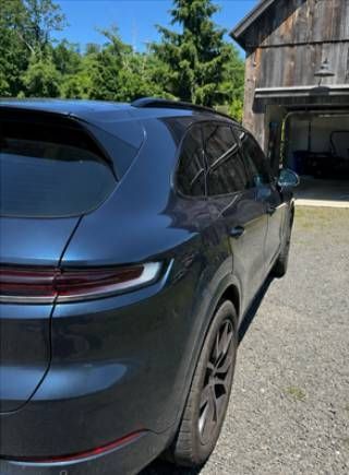 Dark blue SUV parked beside a wooden barn and open garage on a gravel driveway.